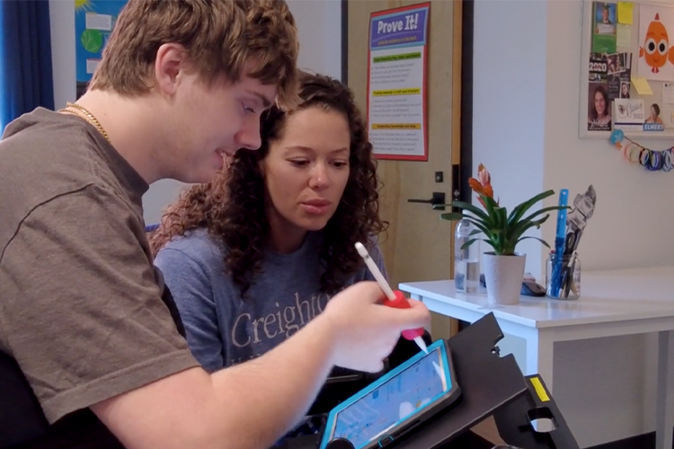 Assistive technology therapist works with a patient to collaborates with a patient to experiment with a foam grip, enabling the individual to hold a stylus while accessing their iPad.