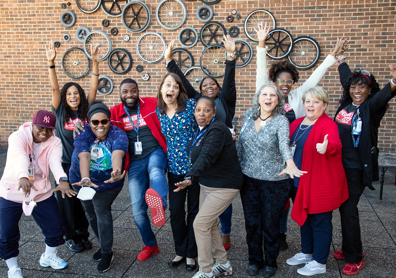 A group of coworkers strike a silly pose for a picture in front of a brick wall adorned with different types of wheels