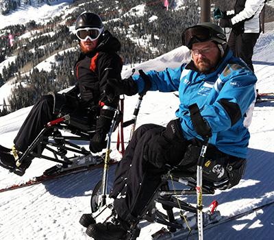 Two participants in Shepherd Center's adaptive ski trip sit on a slope.