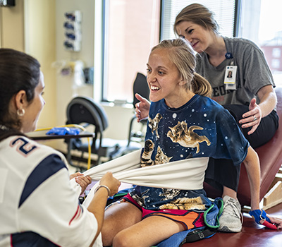 Caroline Moore Broddman, who sustained a spinal cord injury, works with a physical and occupation therapists during a session.