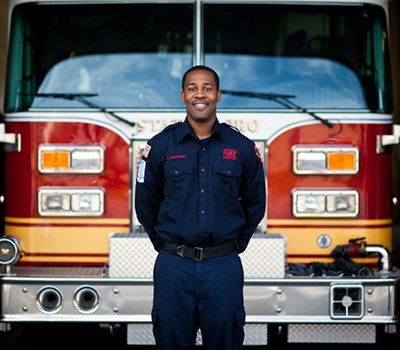 Lamar Matthews-Webb, a firefighter and former brain injury patient, stands in front of a fire truck.