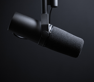A slightly illuminated podcast microphone against a black background.