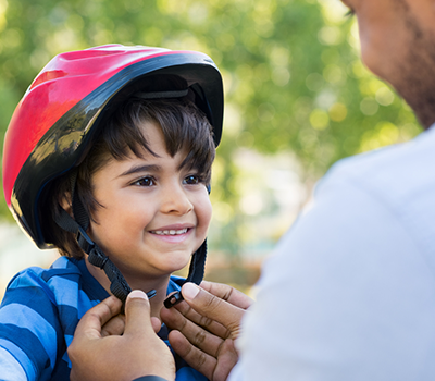 A father helps his cheerful son put on a helmet for a bike ride.