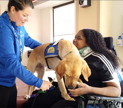 Shanna Thorpe, CTRS, Recreation Therapist, assists an adolescent patient with a Shepherd Center facility dog.
