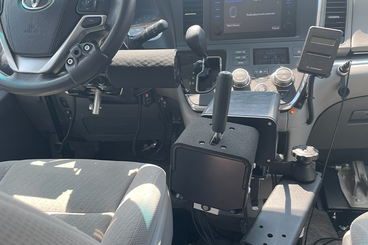 An inside view of an adaptive vehicle equipped with a handstick to the right of the steering wheel enabling a driver to apply the accelerator and breaks by hand.
