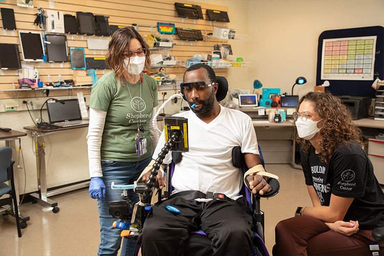 An individual working with therapists while seated in his wheelchair. His cell phone is securely mounted on the armrest for convenient, hands-free access.