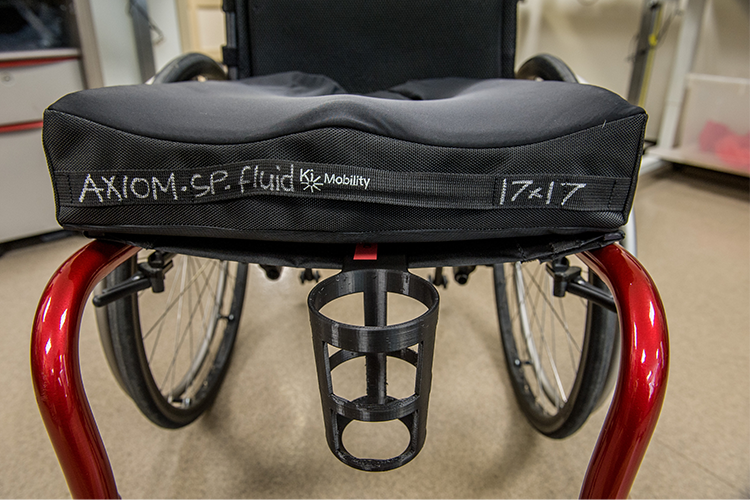 A front perspective of a manual wheelchair featuring a cup holder affixed to the center of the seat frame.