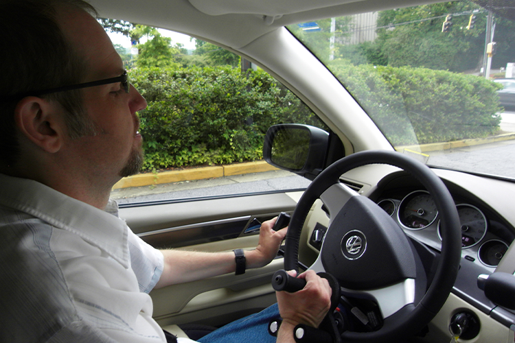 Inside view of a client learning to drive on an adaptive vehicle with a joystick to help control the steering wheel