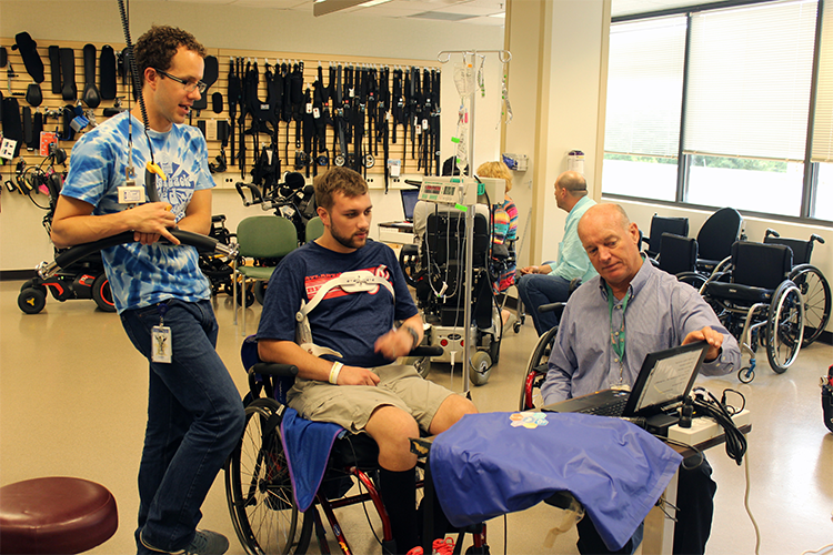 A Shepherd Center patient discusses pressure mapping results with his pair of seating and mobility specialists.