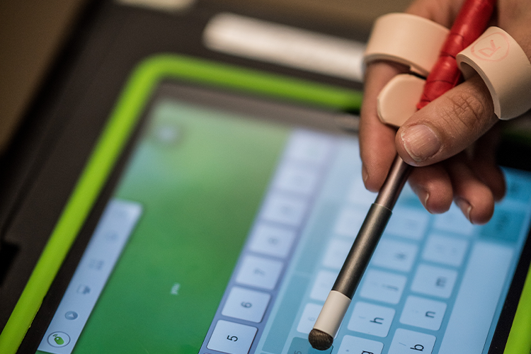 An individual is depicted in close-up using a foam grip to hold a stylus while accessing their iPad.