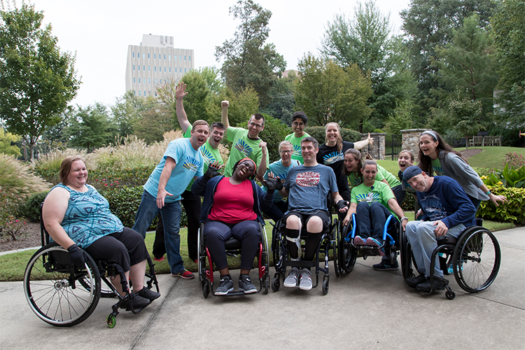 A group of individuals in wheelchairs shares smiles with their therapists outdoors after completing a wheelchair skills clinic.
