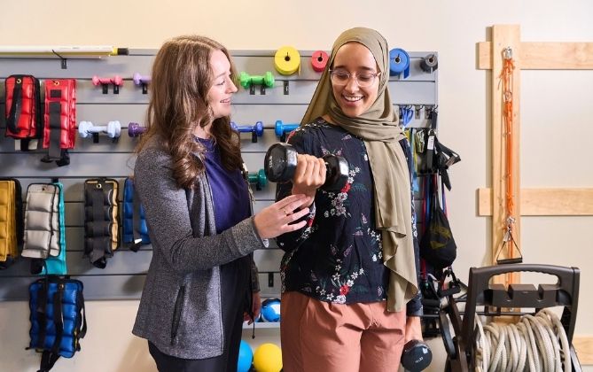 A patient works with Exercise Physiologist Meghan Santander to strengthen her muscles by lifting light weights. Weight training can strengthen weakened muscles caused by multiple sclerosis.