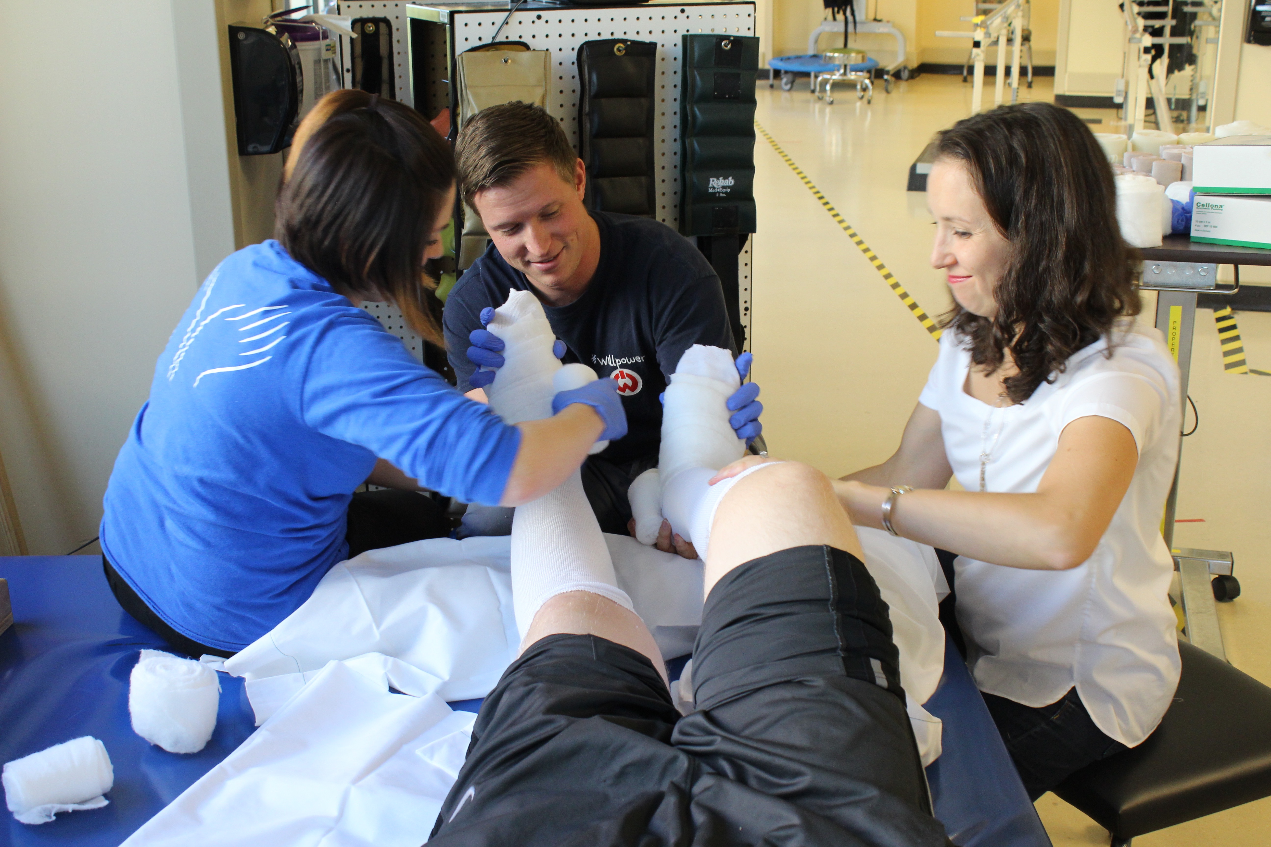 Three therapists change the bandages on a patient's legs