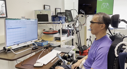A spinal cord injury patient, who has limited mobility in his hands and arms, masters the use of motion sensor glasses in the Access Technology Lab to operate a finance spreadsheet on the desktop computer.