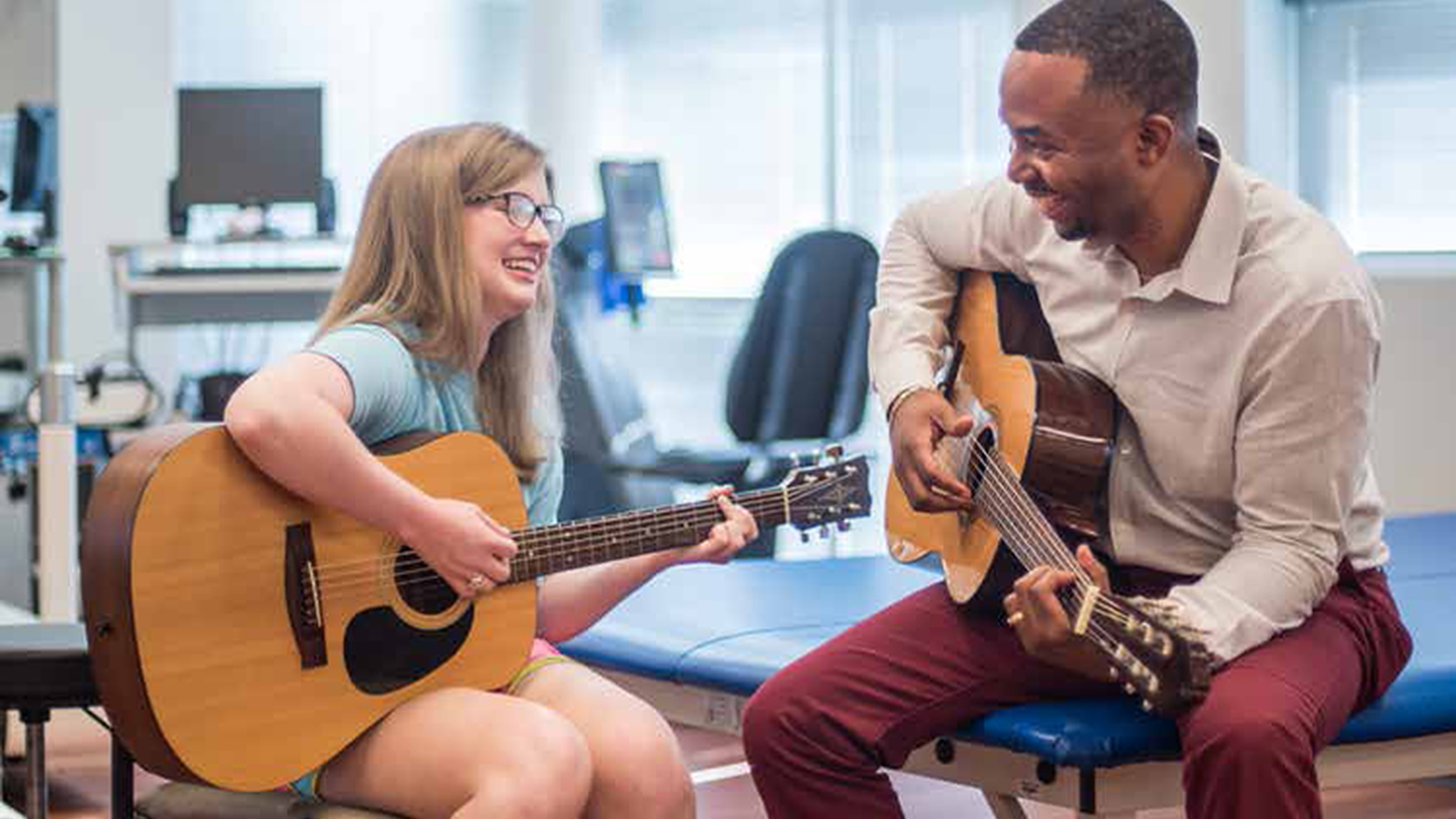 Patient and her therapist smile as they play guitar together as part of their brain injury therapy