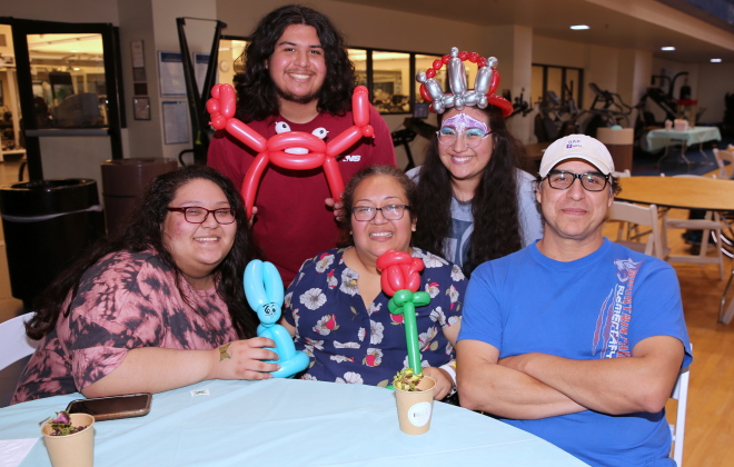A group of family members and caregivers sport various balloon animals and crowns at a peer support event.