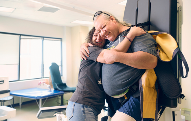 Physical therapists gives her patient a big hug while he is using the Eirgo machine to improve upright tolerence,