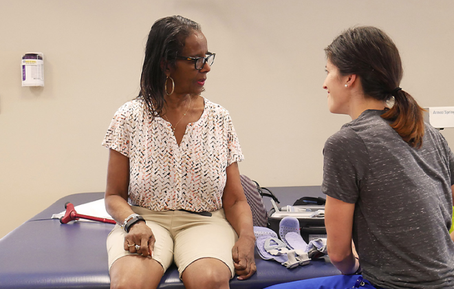 Pathways patient sits on therapy table while discussing care with her physical therapist