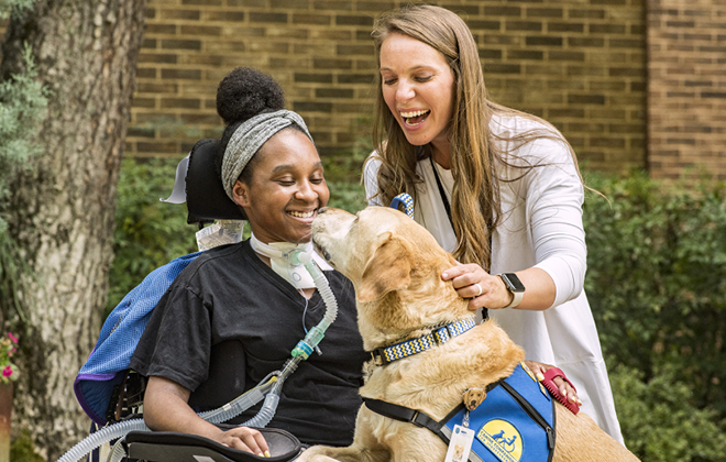 Patient using a wheelchair smiling as she greets one of Shepherd's facility dogs