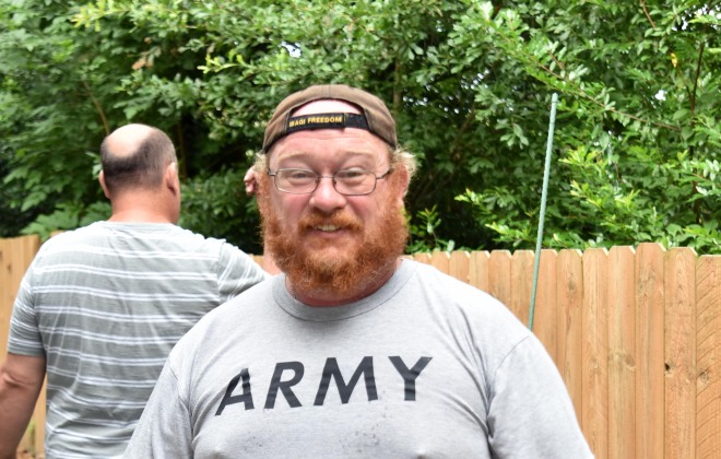 A client from the SHARE Military Initiative smiles while gardening. He is wearing a t-shirt that reads, "Army."