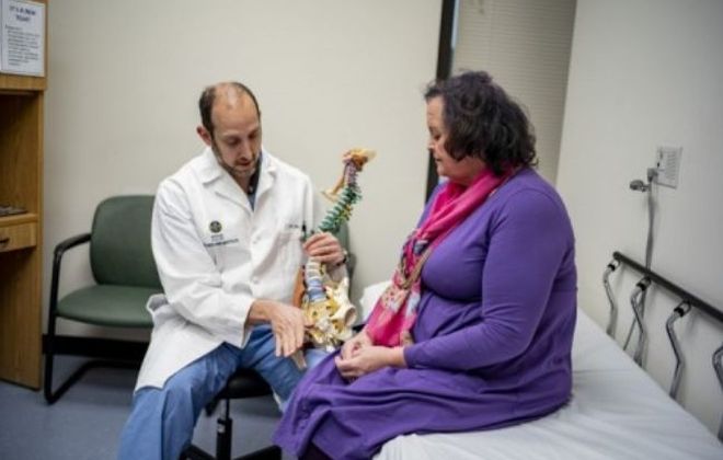 A Pain Institute physician points to a model spine while sitting next to a female patient