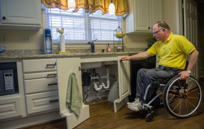 Former patient, Ken Johnson, showcases his lowered cabinets beneath his kitchen sink as part of his transition back to his home. The false cabinet fronts help accommodate his wheelchair.