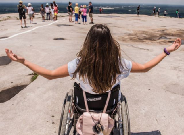 Woman sitting in a wheelchair with arms out to her side on top of a mountain.