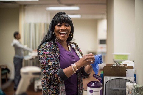 Smiling nurse puts on gloves to assist with patient treatment