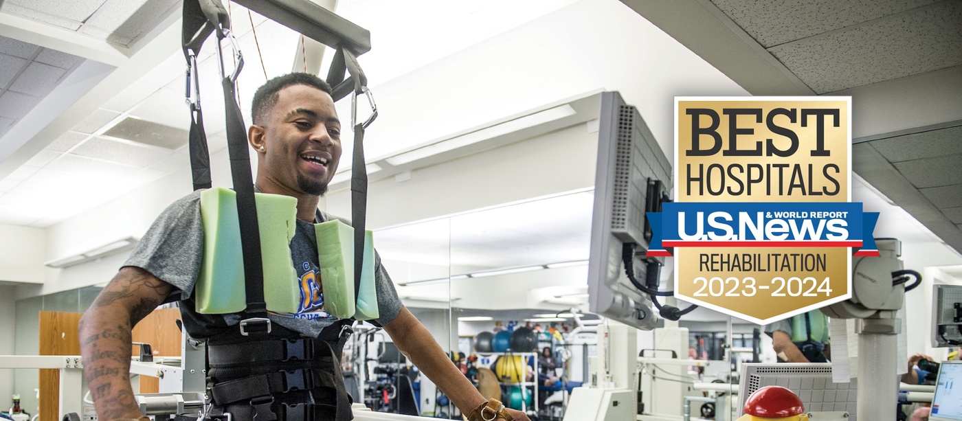 Shepherd Center patient smiles while using therapeutic equipment for lower-limb muscle strength. The U.S. News badge is overlayed with the words, "Best Hospitals Rehabilitation 2022-23."