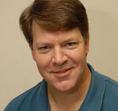 Headshot of Chris Nesbitt, MPT,  smiling from the shoulders up wearing a blue polo